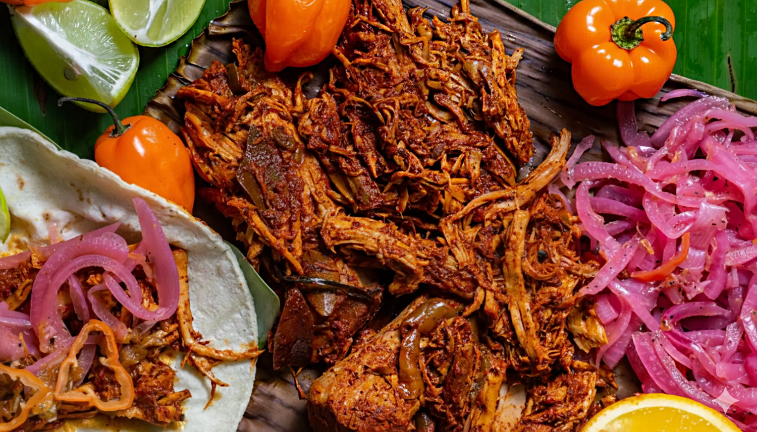 A steaming plate of Cochinita Pibil, tender pork wrapped in banana leaves, garnished with pickled red onions and fresh habanero chilies on a vibrant Yucatecan tablecloth.