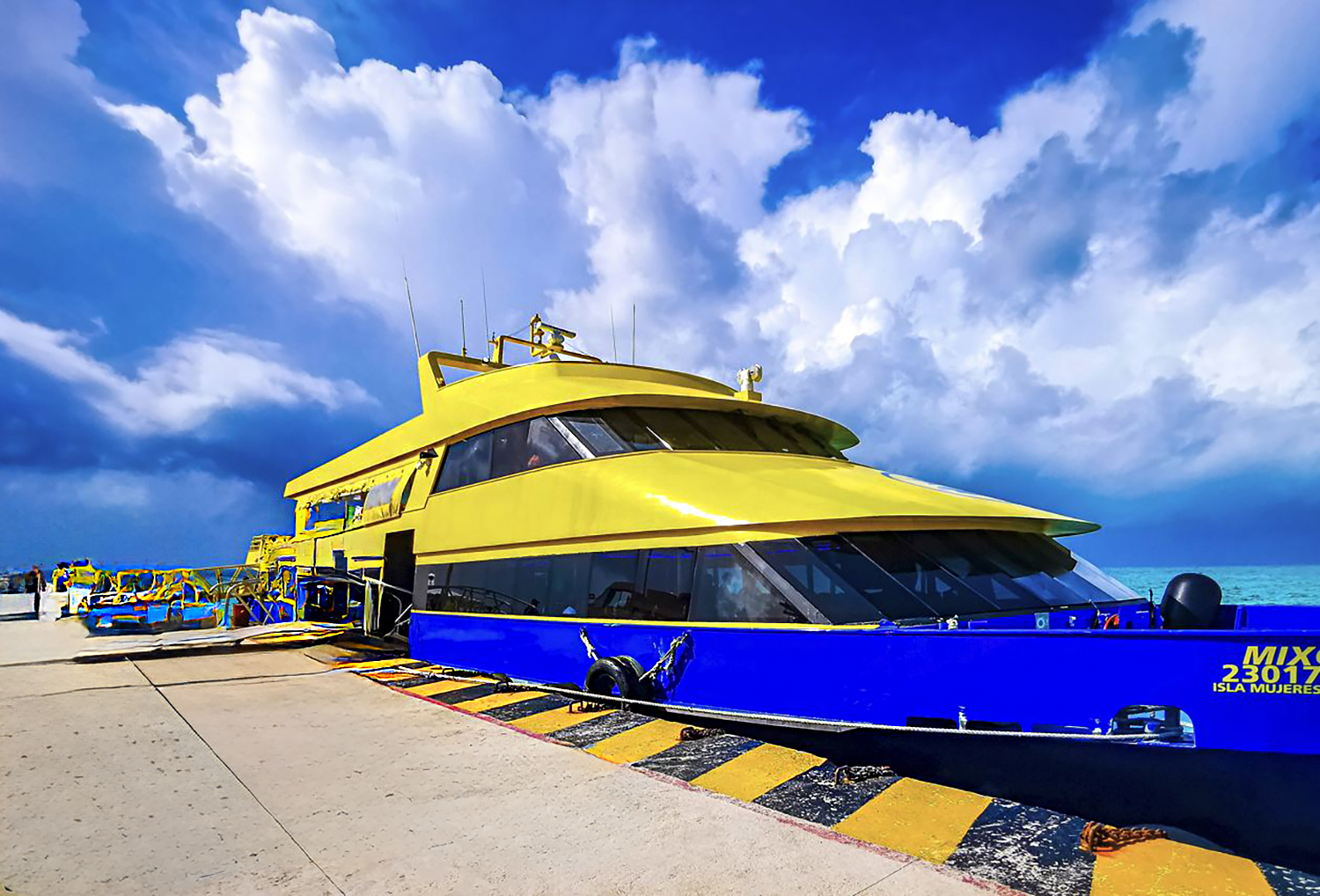 A ferry boat sailing from Cancún toward the turquoise waters and white sands of Isla Mujeres under a clear blue sky.