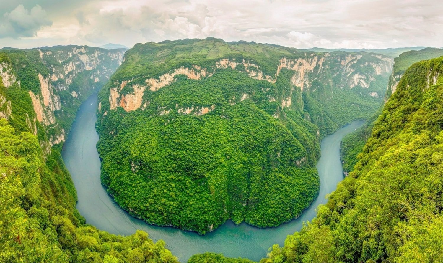 Towering vertical cliffs of Cañón del Sumidero rising dramatically above the winding Grijalva River, surrounded by lush vegetation in Chiapas, Mexico